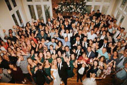 Large group of wedding guests posing together in the reception hall at The Estate at Sunset Farm
